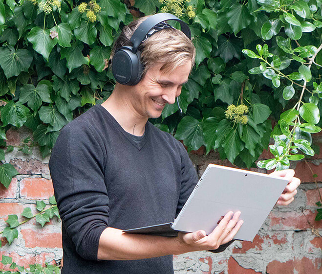 hero - Someone standing outside in front of a brick wall with ivy, holding a Surface laptop, using Microsoft Teams