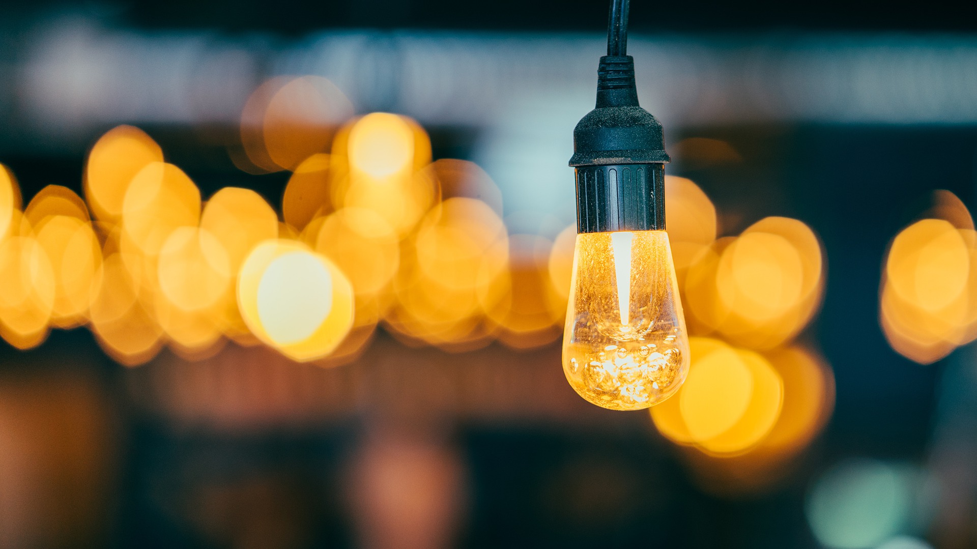 news - A modern looking lightbulb hanging in front of blurry lights in the background