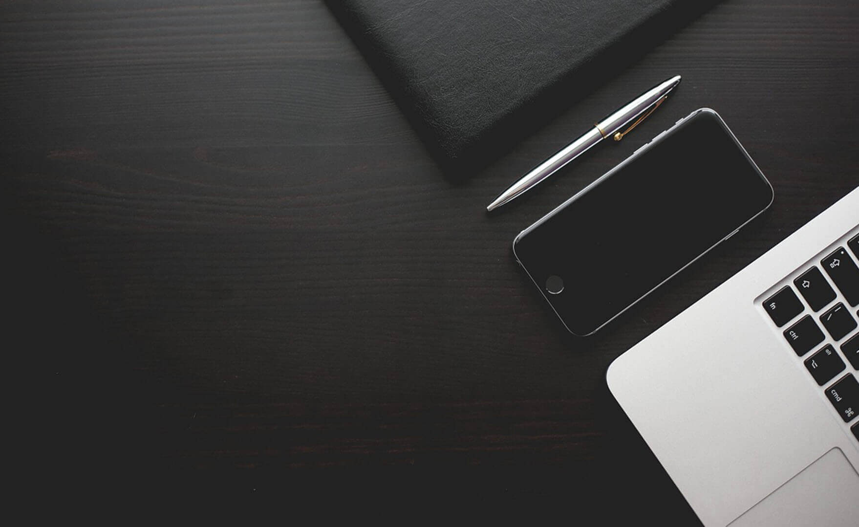 news - A stylish dark desktop with a pen, a laptop and a phone arranged on it