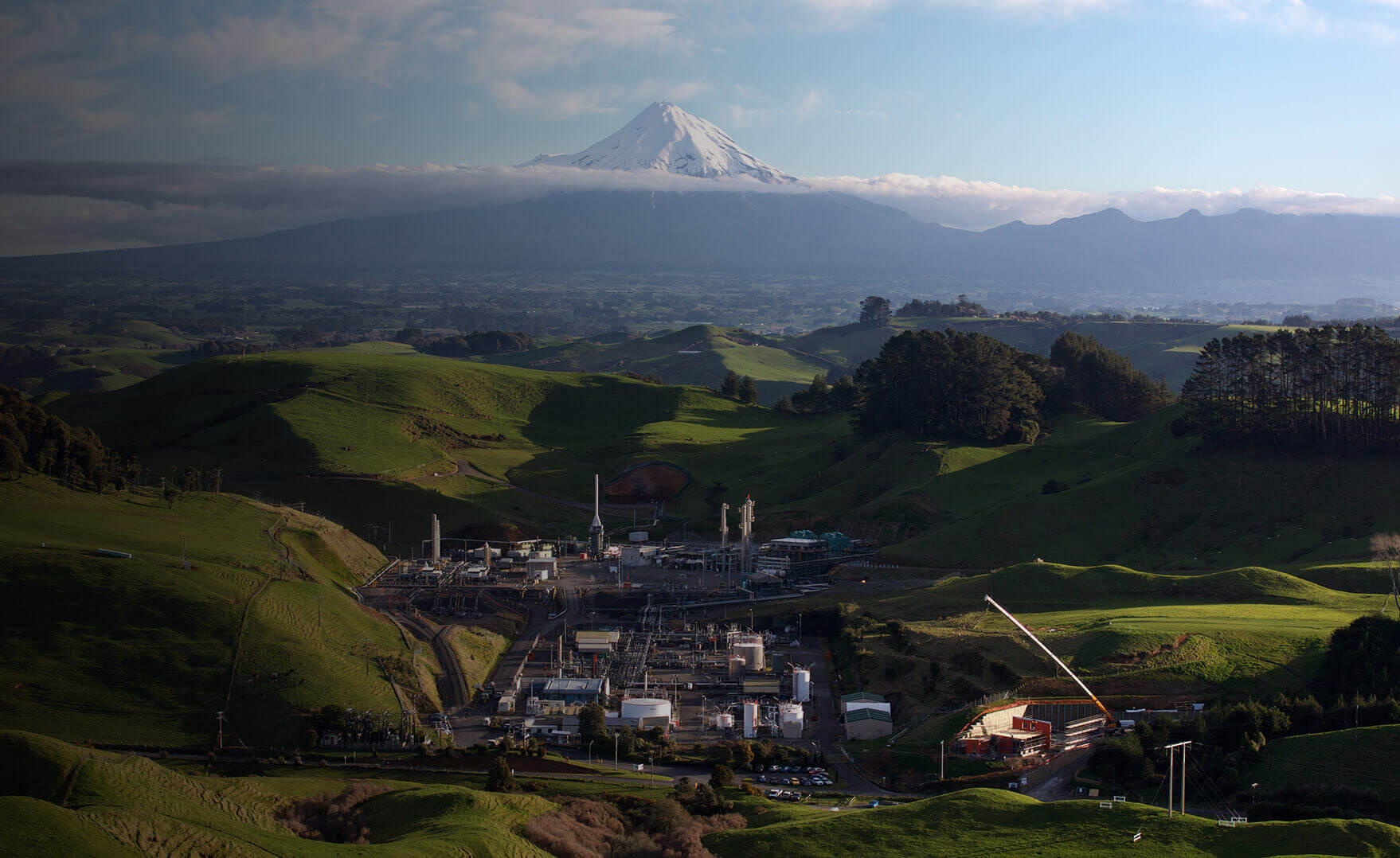 news shadow - A Todd Energy manufacturing plant sitting among green hills with Mount Taranaki in the background